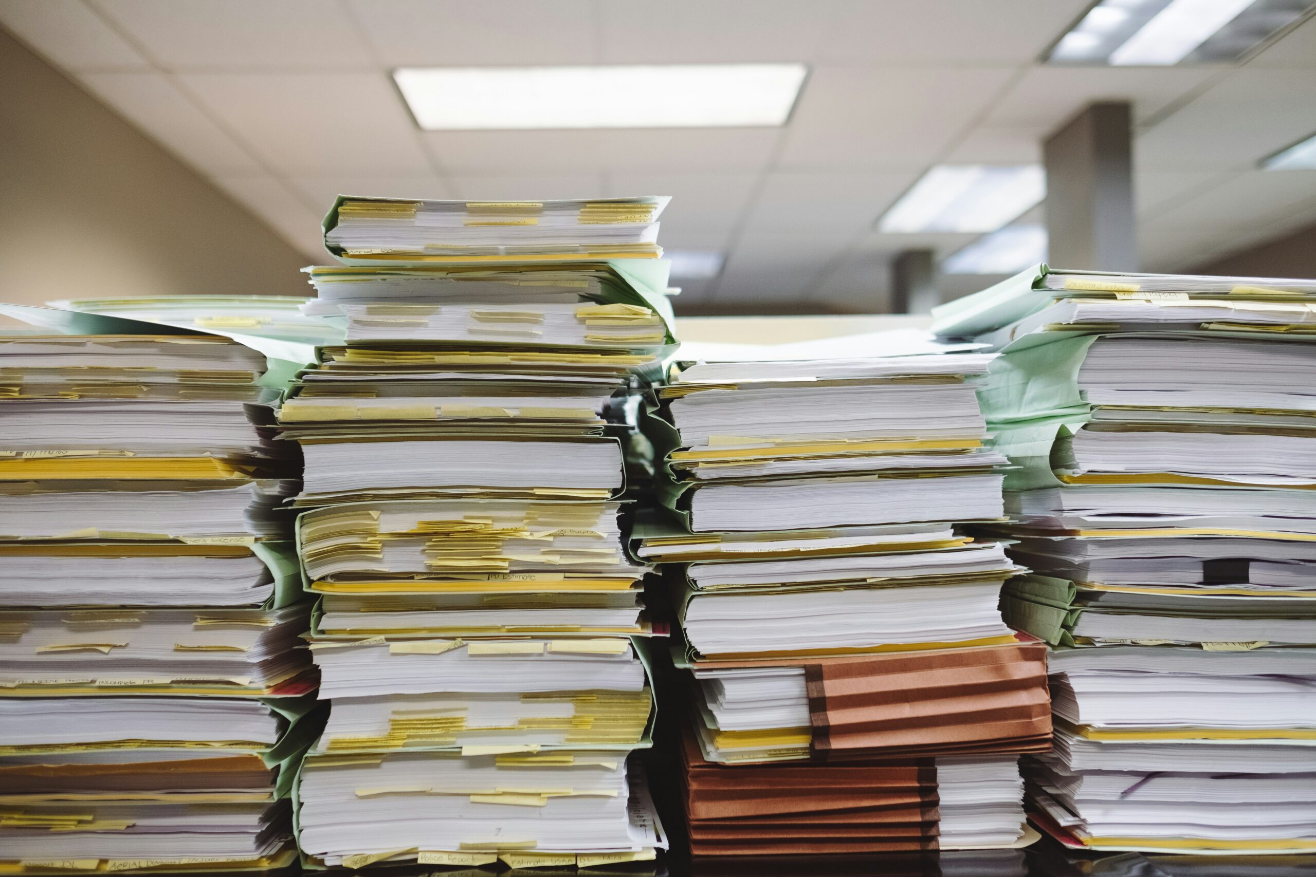 Stack of organized legal patent documents on a desk next to a laptop
